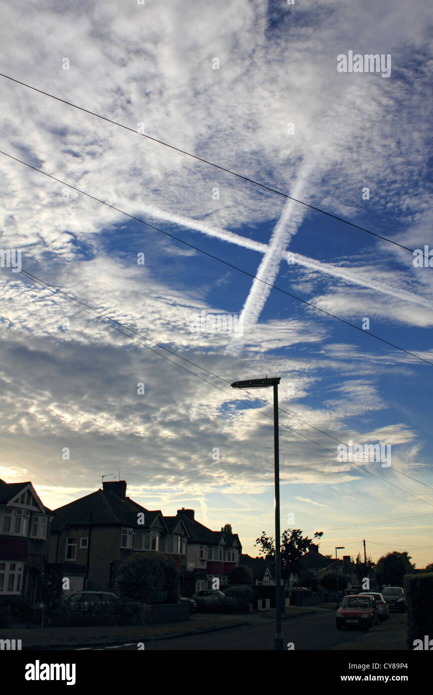 X nel cielo creato da due piano contrails sopra di attraversamento strada suburbana nel Surrey in Inghilterra REGNO UNITO Foto Stock