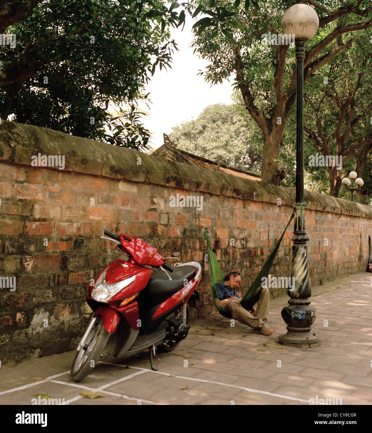 Street Photography - uomo dorme in una scena di strada ad Hanoi nel Vietnam del Sud-est asiatico in Estremo Oriente. Ciclomotore Vespa Foto Stock
