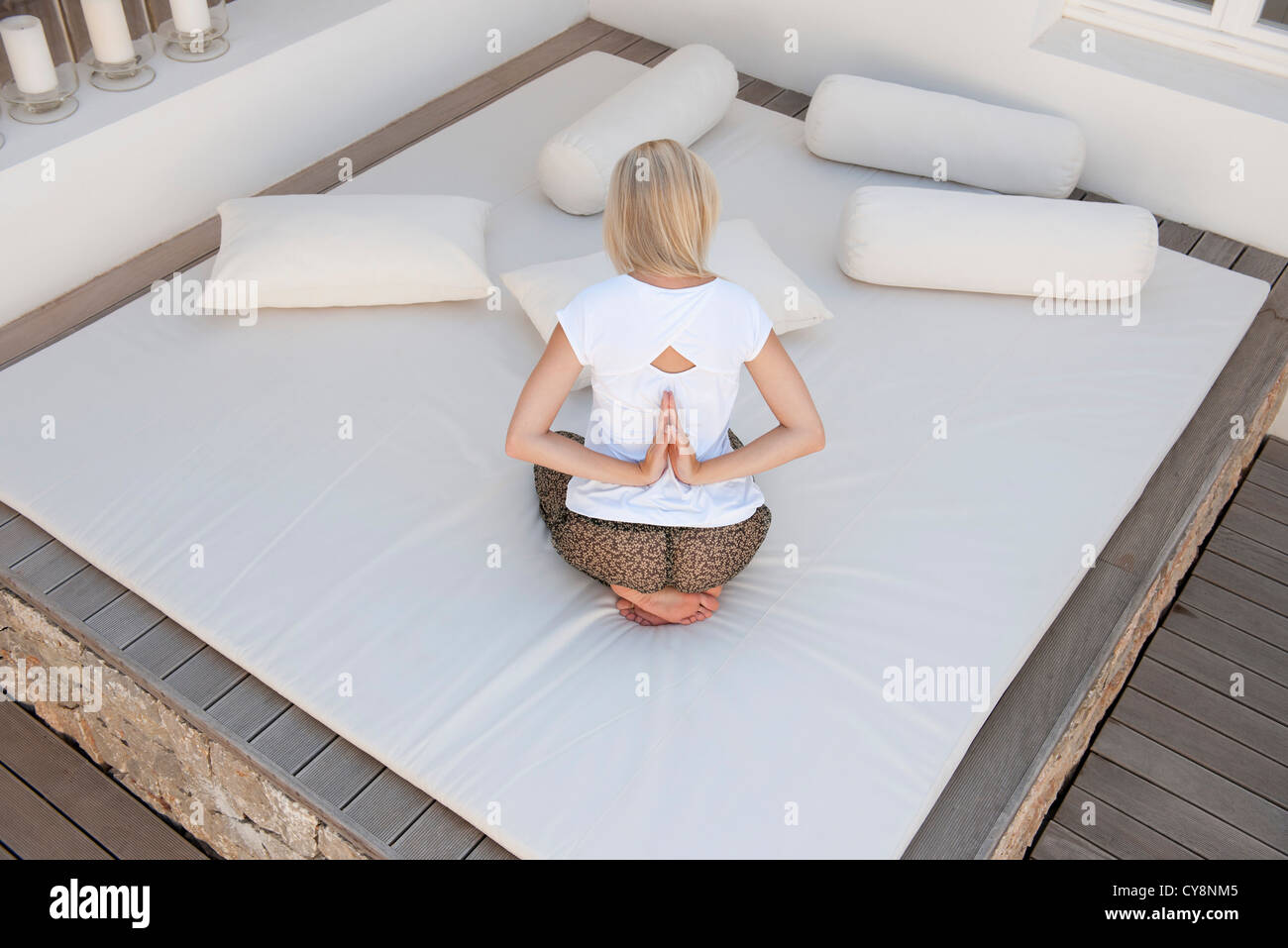 Donna facendo retromarcia preghiera pone sul letto nel patio, vista posteriore Foto Stock
