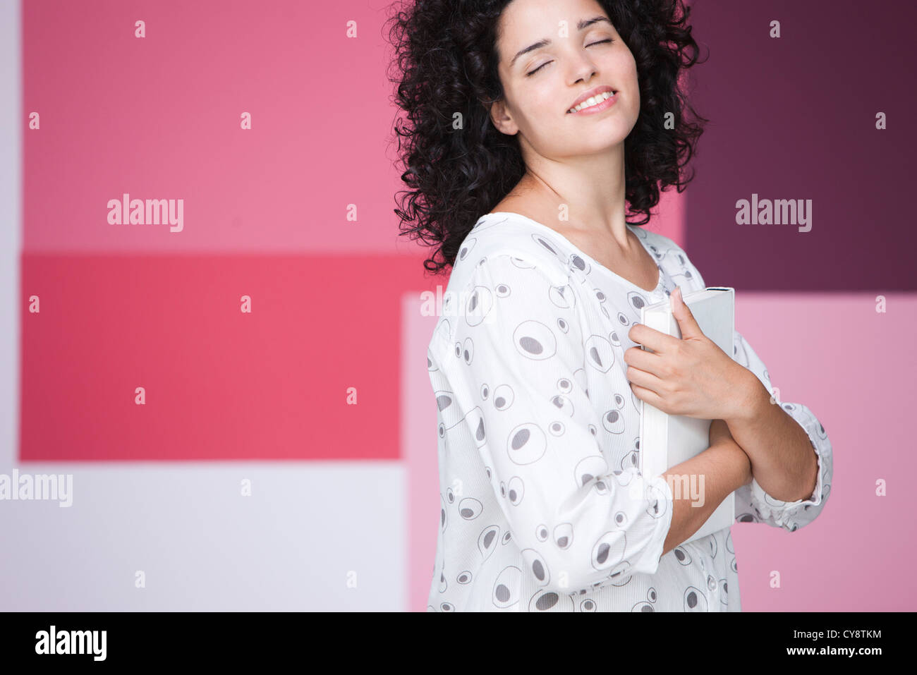 Giovane donna azienda prenota al petto con gli occhi chiusi, sorridente Foto Stock