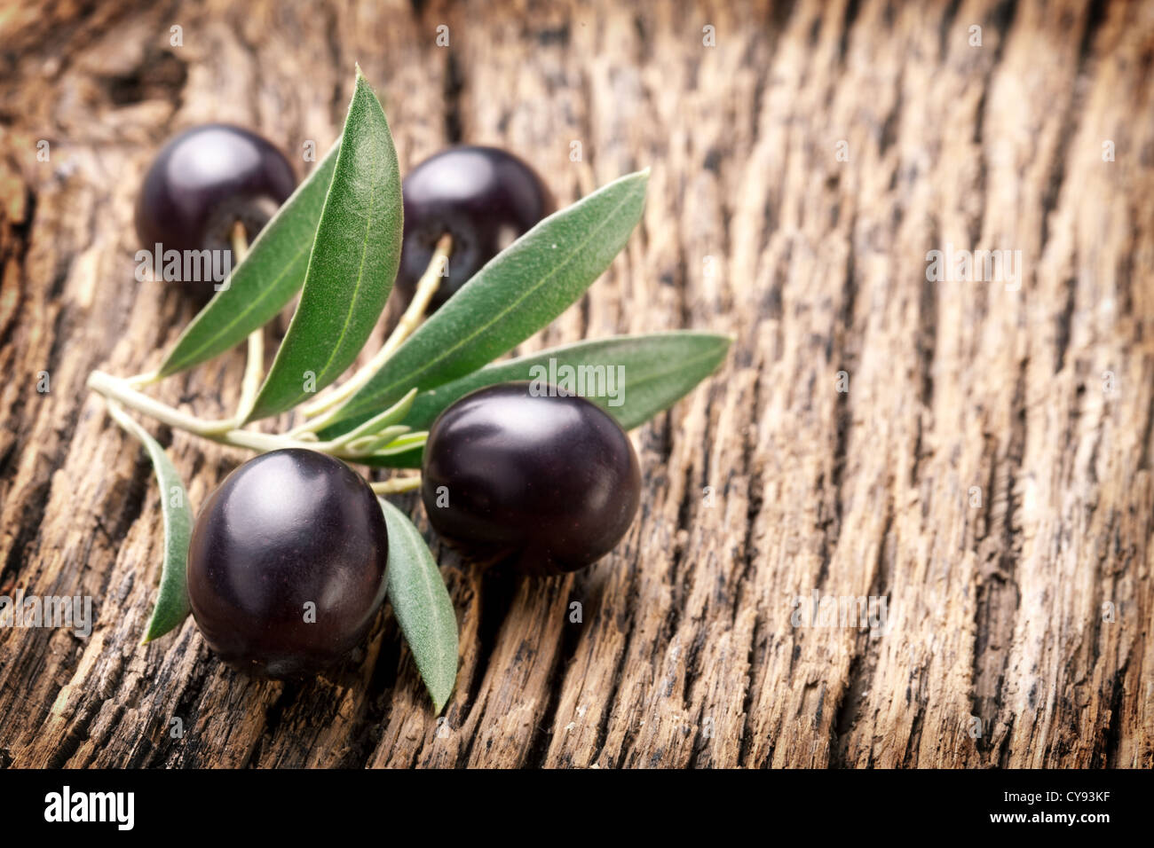 Mature olive nere con foglie su un sfondo di legno. Foto Stock