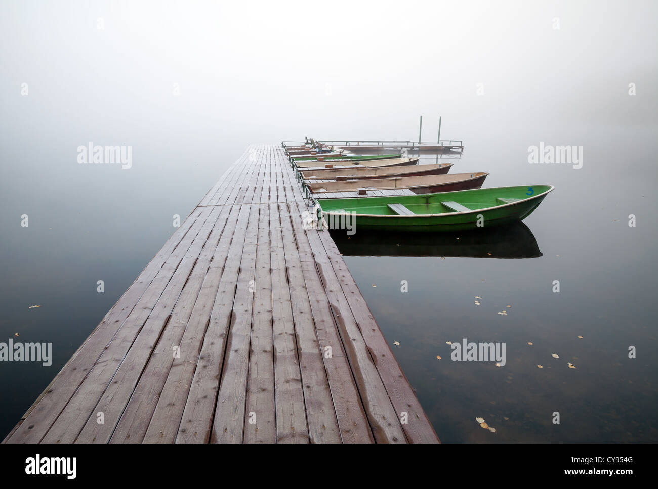 L'autunno. Piccolo molo con barche sul lago in ancora fredda mattinata nebbiosa Foto Stock