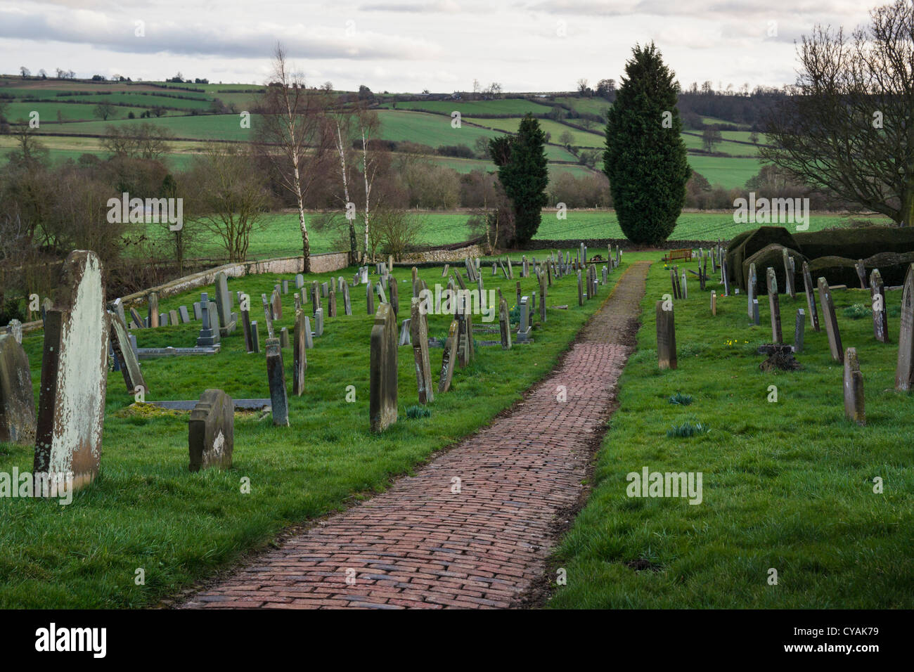 Il cimitero presso la chiesa di San Michele a Coxwold con un vecchio sentiero acciottolato e North Yorkshire paesaggio come sfondo. Foto Stock