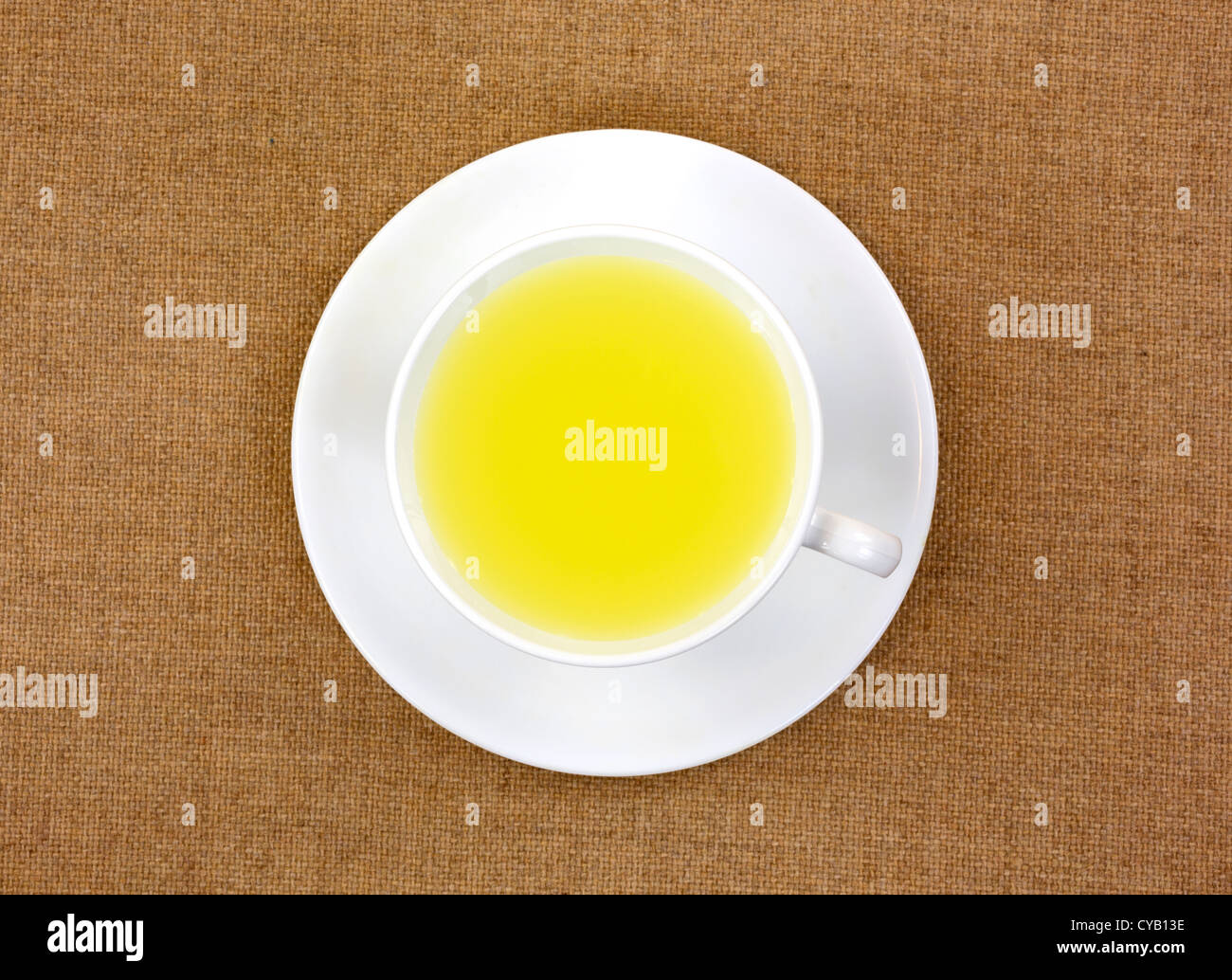 Vista superiore del succo di limone in una tazza bianca con piattino su un panno marrone chiaro dello sfondo. Foto Stock