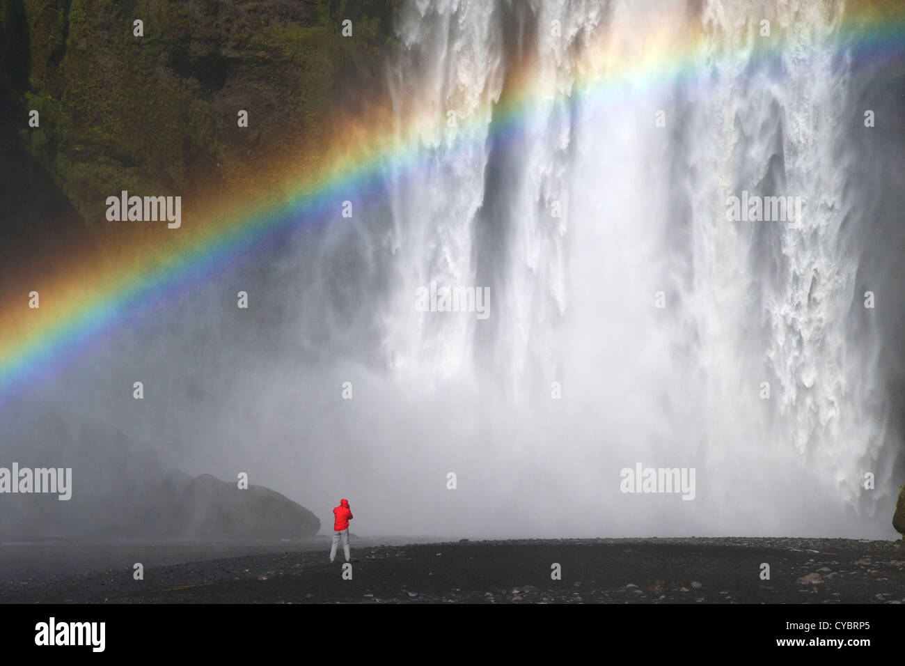 Una persona di fotografare Skogafoss cascata con arcobaleno nel sole estivo, South Coast, Islanda Foto Stock