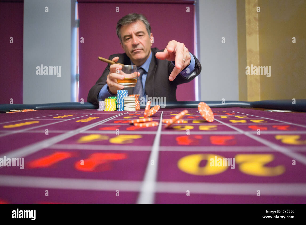 Uomo seduto a tavola tenendo un sigaro gettando chips Foto Stock