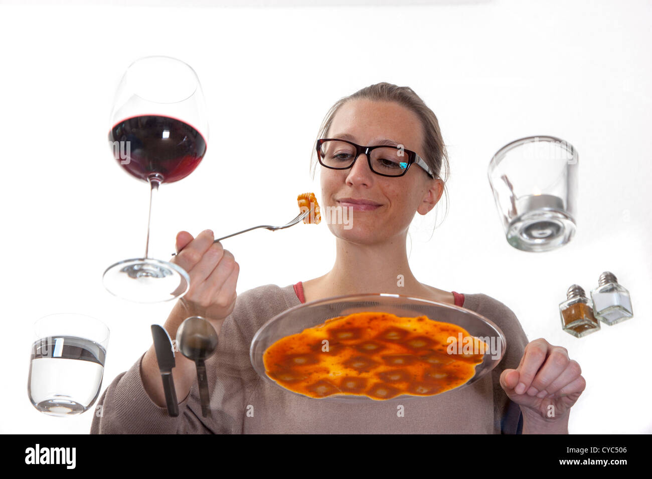 Giovane donna è seduta al tavolo di vetro. Mangiare pasta, ravioli con una salsa di pomodoro, acqua minerale e un bicchiere di vino rosso. Foto Stock