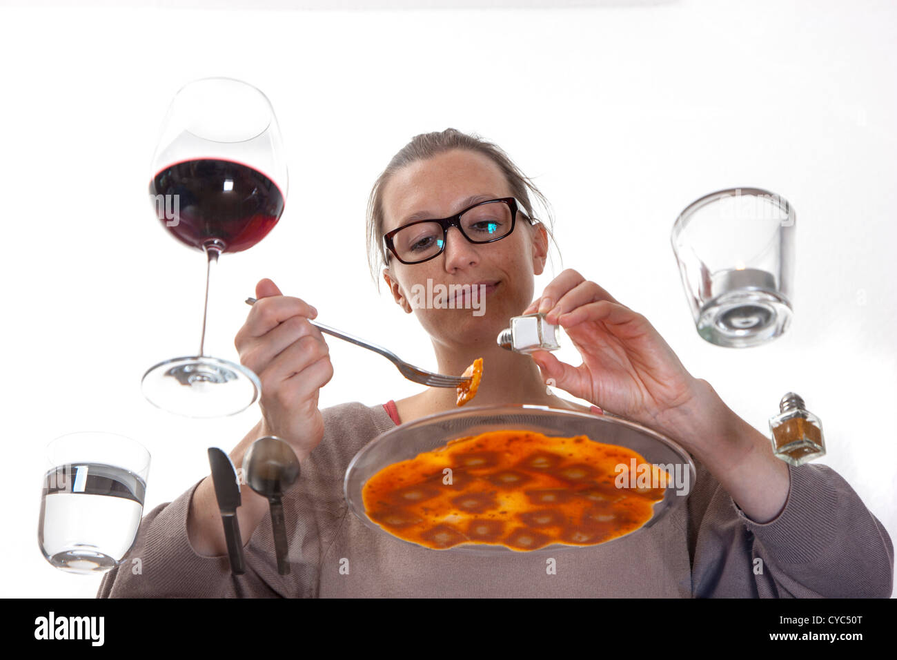 Giovane donna è seduta al tavolo di vetro. Mangiare pasta, ravioli con una salsa di pomodoro, acqua minerale e un bicchiere di vino rosso. Foto Stock