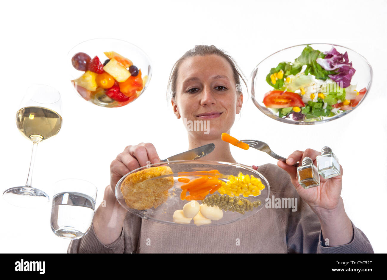 Giovane donna è seduta al tavolo di vetro. Mangiare un pasto, Schnitzel, patate, verdure, insalata mista, insalata di frutta, vino bianco. Foto Stock