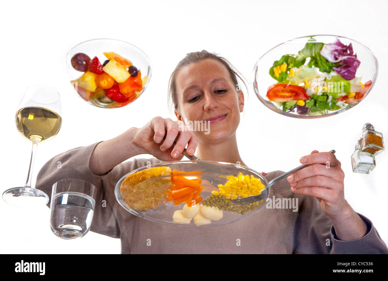 Giovane donna è seduta al tavolo di vetro. Mangiare un pasto, Schnitzel, patate, verdure, insalata mista, insalata di frutta, vino bianco. Foto Stock