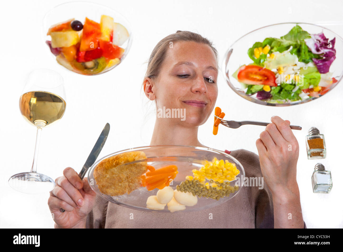 Giovane donna è seduta al tavolo di vetro. Mangiare un pasto, Schnitzel, patate, verdure, insalata mista, insalata di frutta, vino bianco. Foto Stock