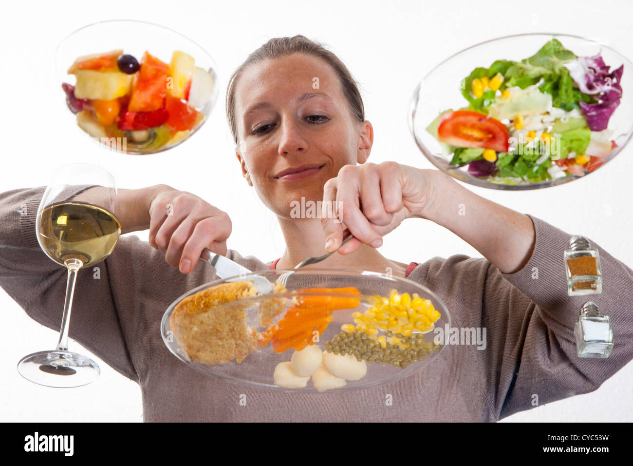 Giovane donna è seduta al tavolo di vetro. Mangiare un pasto, Schnitzel, patate, verdure, insalata mista, insalata di frutta, vino bianco. Foto Stock
