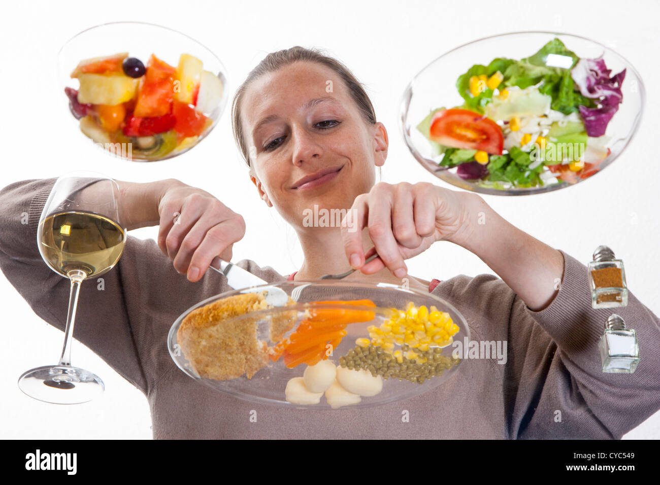 Giovane donna è seduta al tavolo di vetro. Mangiare un pasto, Schnitzel, patate, verdure, insalata mista, insalata di frutta, vino bianco. Foto Stock