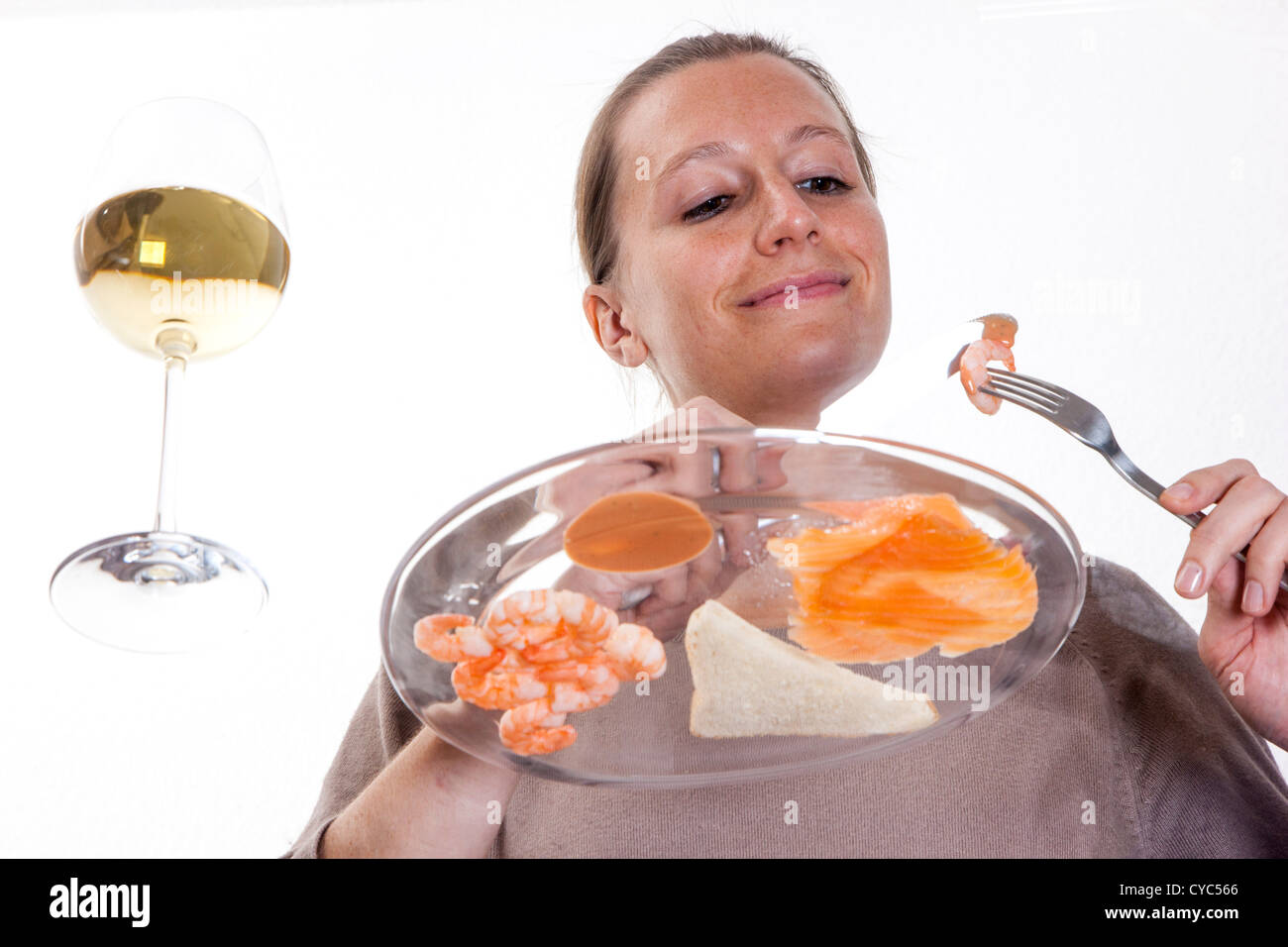 Giovane donna è mangiare a un tavolo di vetro. Salmone affumicato un gamberetti con un bicchiere di vino bianco, toast e un cocktail di vestirsi. Foto Stock