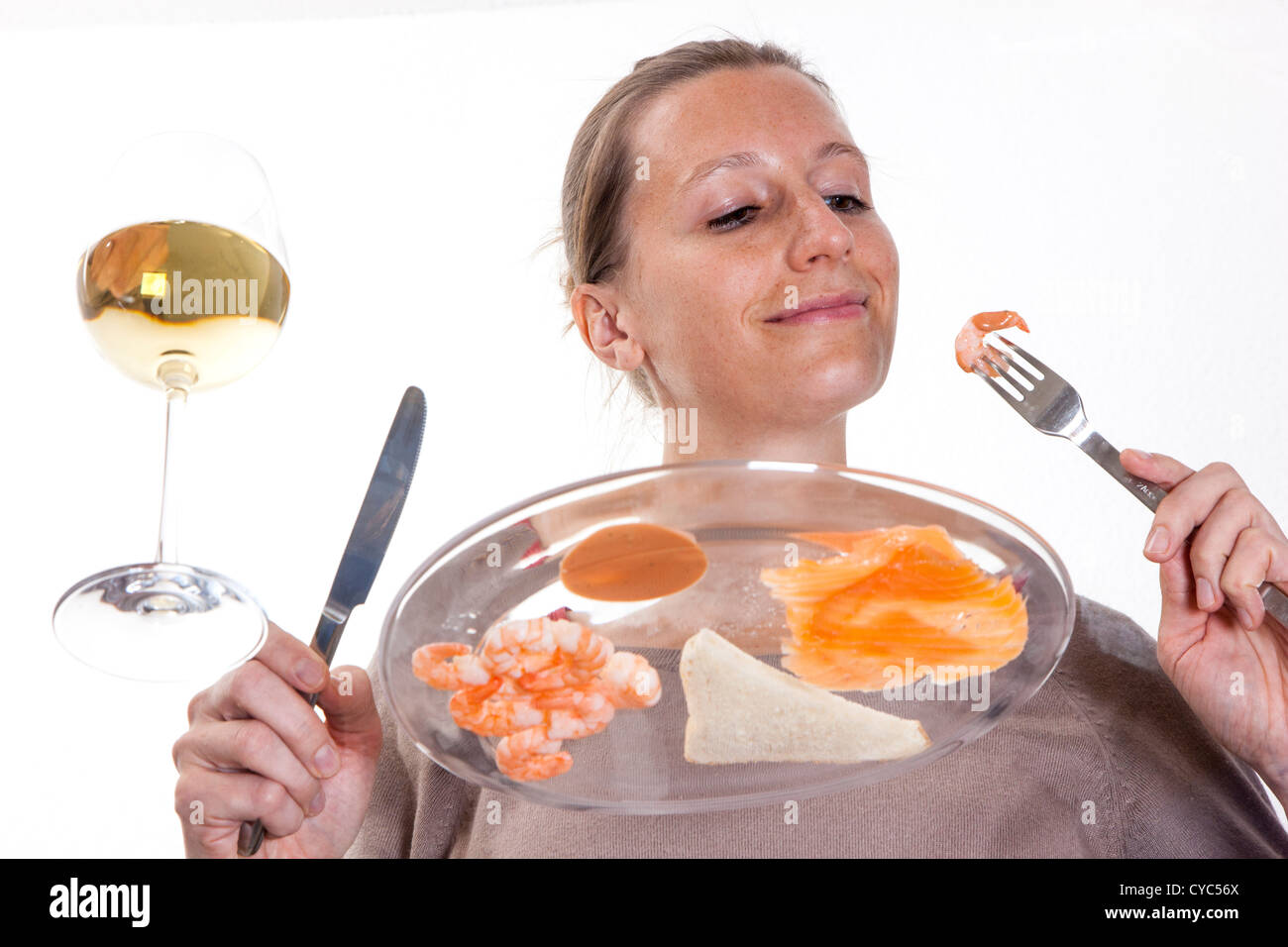 Giovane donna è mangiare a un tavolo di vetro. Salmone affumicato un gamberetti con un bicchiere di vino bianco, toast e un cocktail di vestirsi. Foto Stock