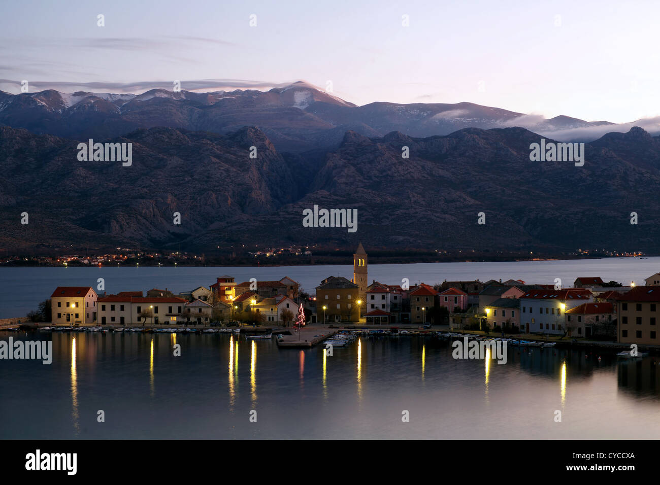 Piccola città costiera di Vinjerac in Croazia al mattino presto con mare calmo, riflessi in acqua e montagne sullo sfondo. Foto Stock