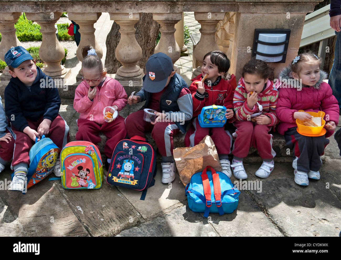 I bambini piccoli mangiano i loro pranzi al sacco durante un viaggio scolastico al President's Kitchen Garden, Attard, Malta Foto Stock