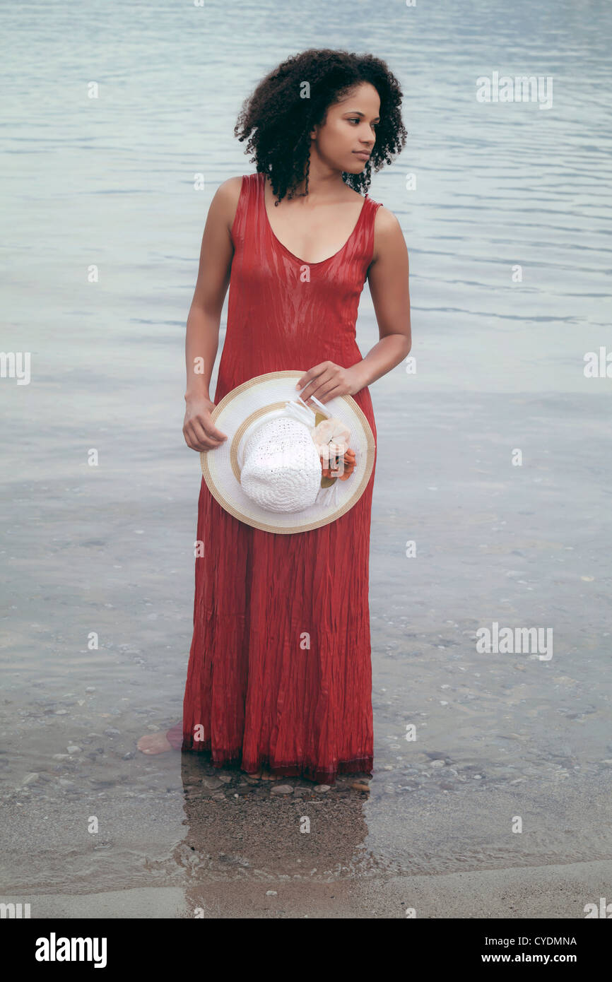 Una ragazza in un abito rosso con un cappello per il sole in piedi in acqua Foto Stock