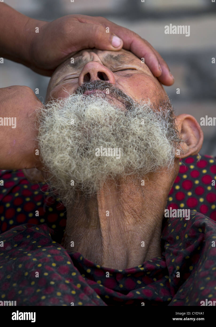 Uyghur uomo Getting rasato da un barbiere a Serik Buya Mercato, Yarkand, Xinjiang Uyghur Regione autonoma, Cina Foto Stock