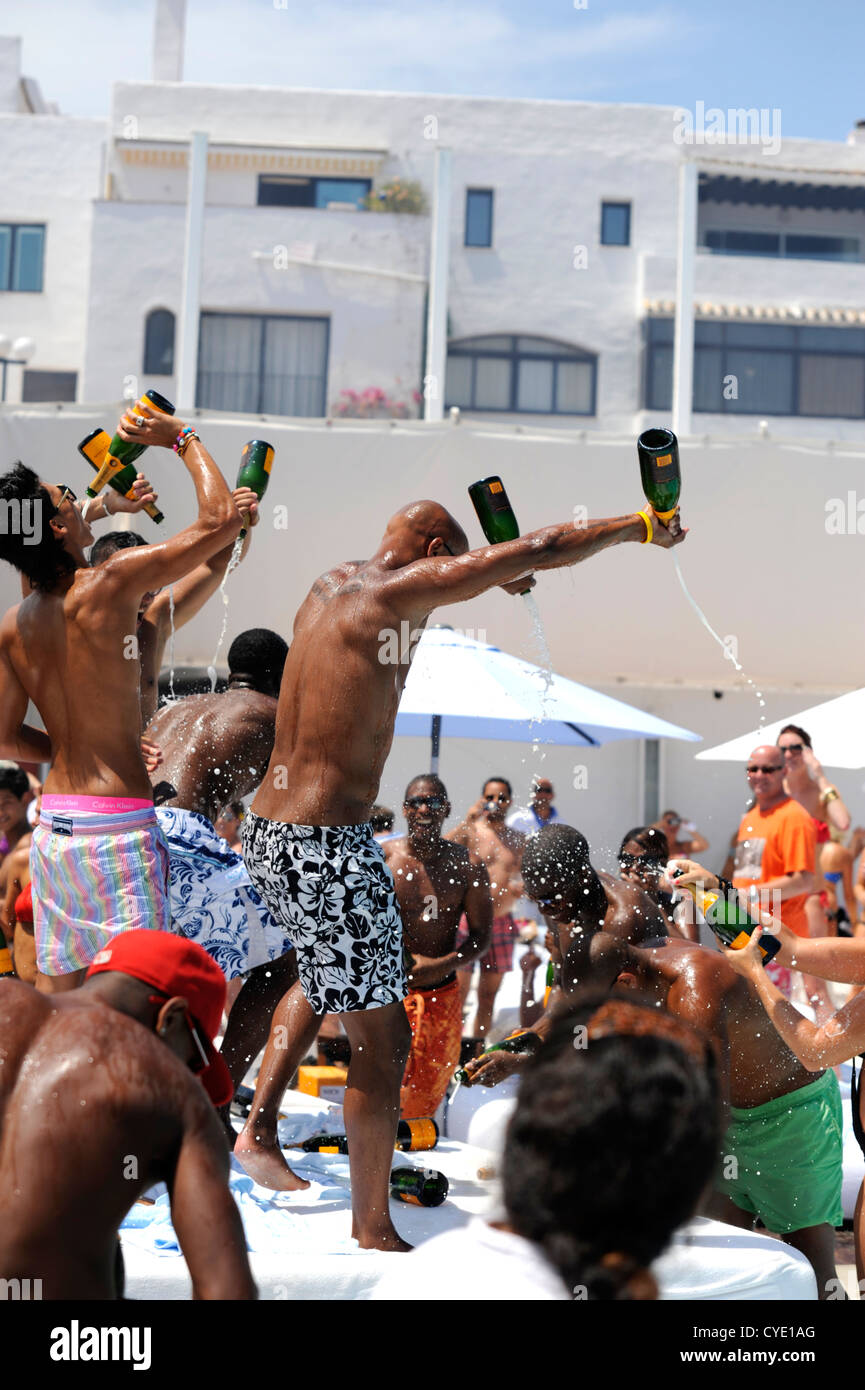 Frequentatori del partito presso il beach club spray champagne party, bere da bottiglie di vueve cliquot e versarli sopra ogni altro Foto Stock