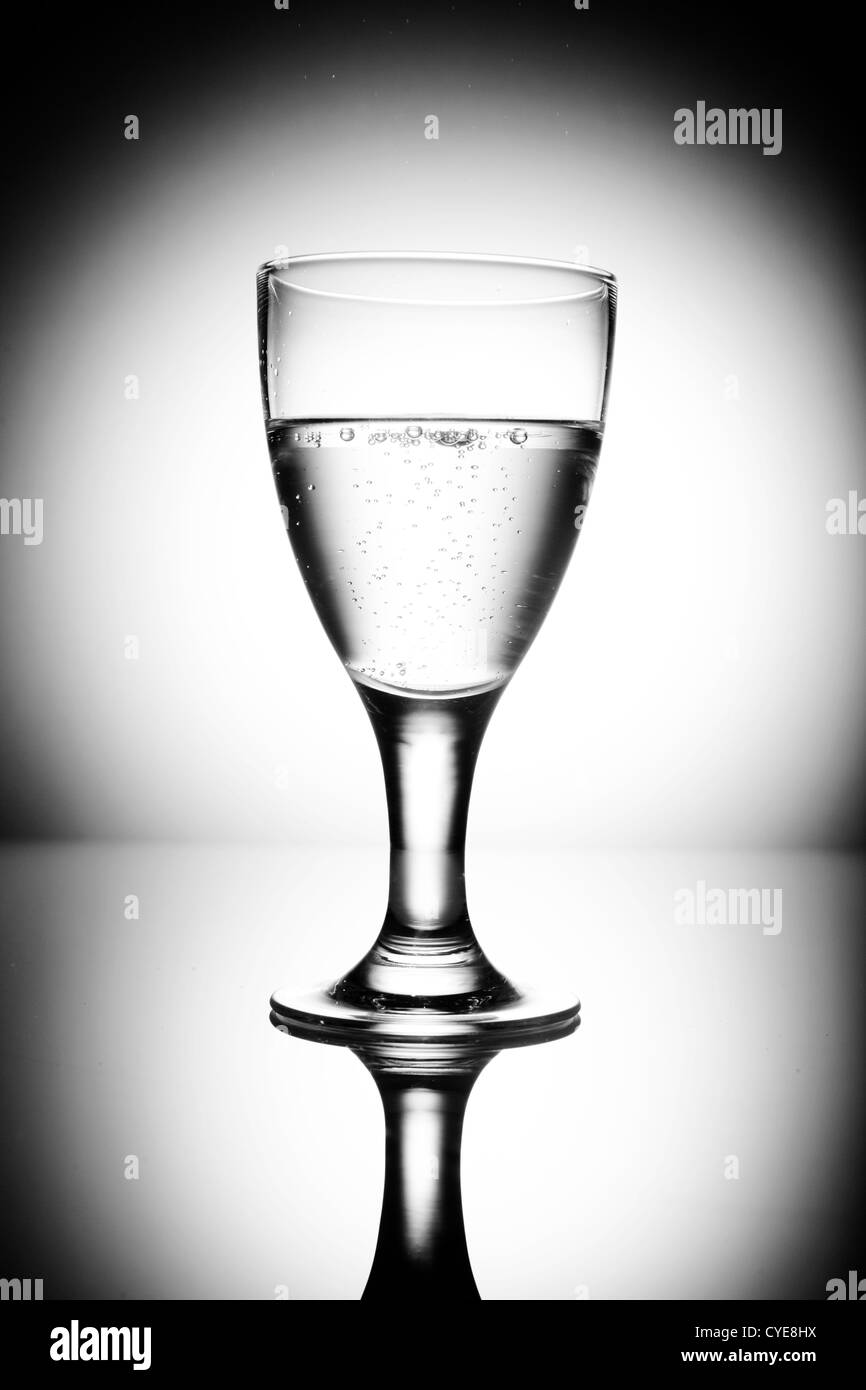 Bicchiere di acqua sul terreno riflettente blu scintillante Foto Stock