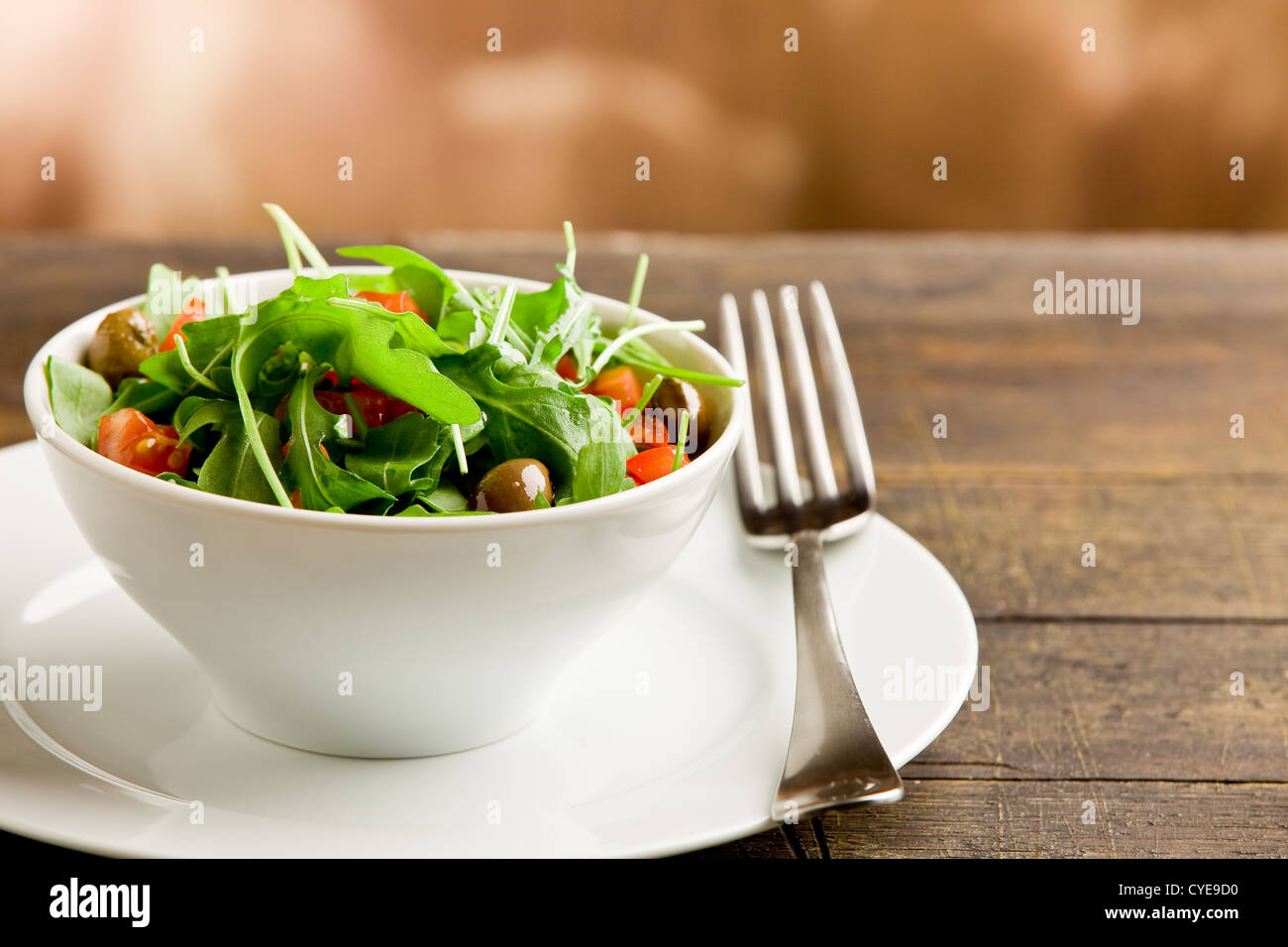 Foto di deliziosa luce con insalata di rucola e pomodori in bianco ciotola sul tavolo di legno Foto Stock