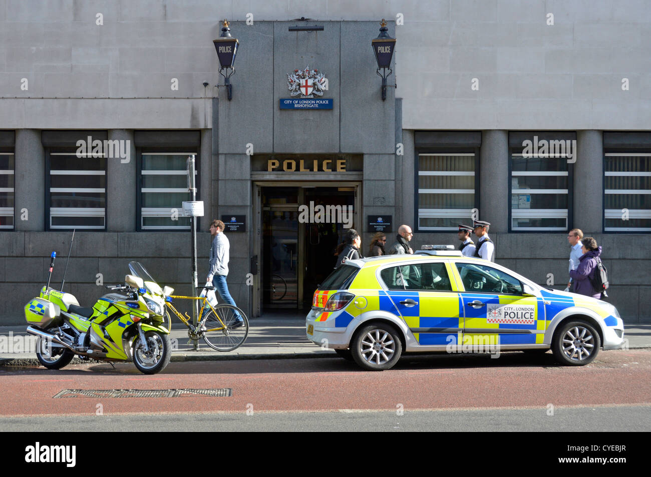 Gli ufficiali di polizia in uniforme accanto alla polizia parcheggiate auto & moto al di fuori della città di Londra Bishopsgate stazione di polizia entrata con estranei passanti Foto Stock