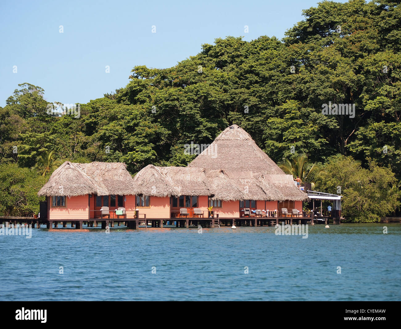 Resort tropicale con bungalow con tetto in paglia sull'acqua e lussureggianti alberi in background, America centrale e di Panama Foto Stock