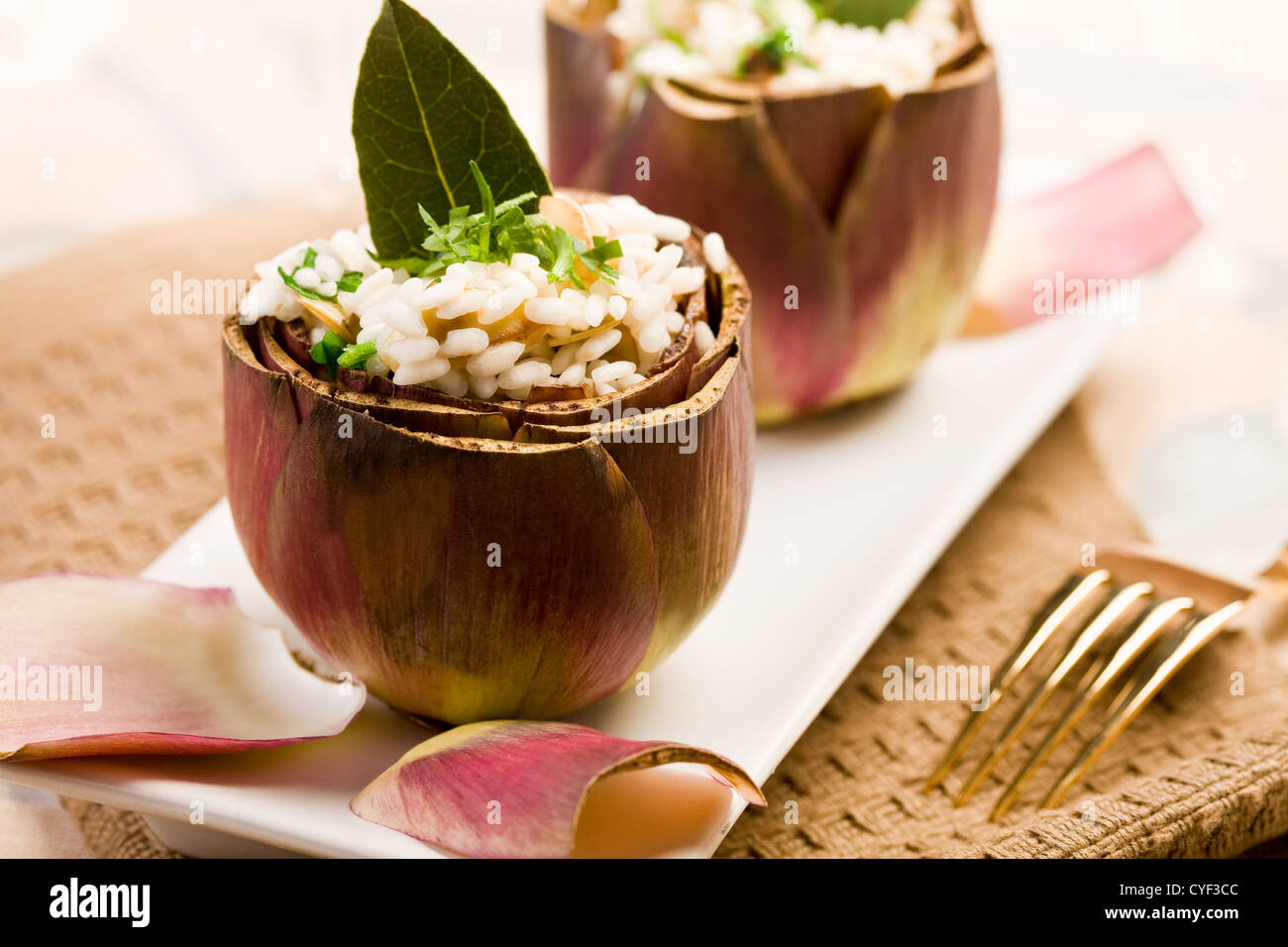 Carciofi Ripieni con risotto sul tavolo elegante con forca d'oro Foto Stock