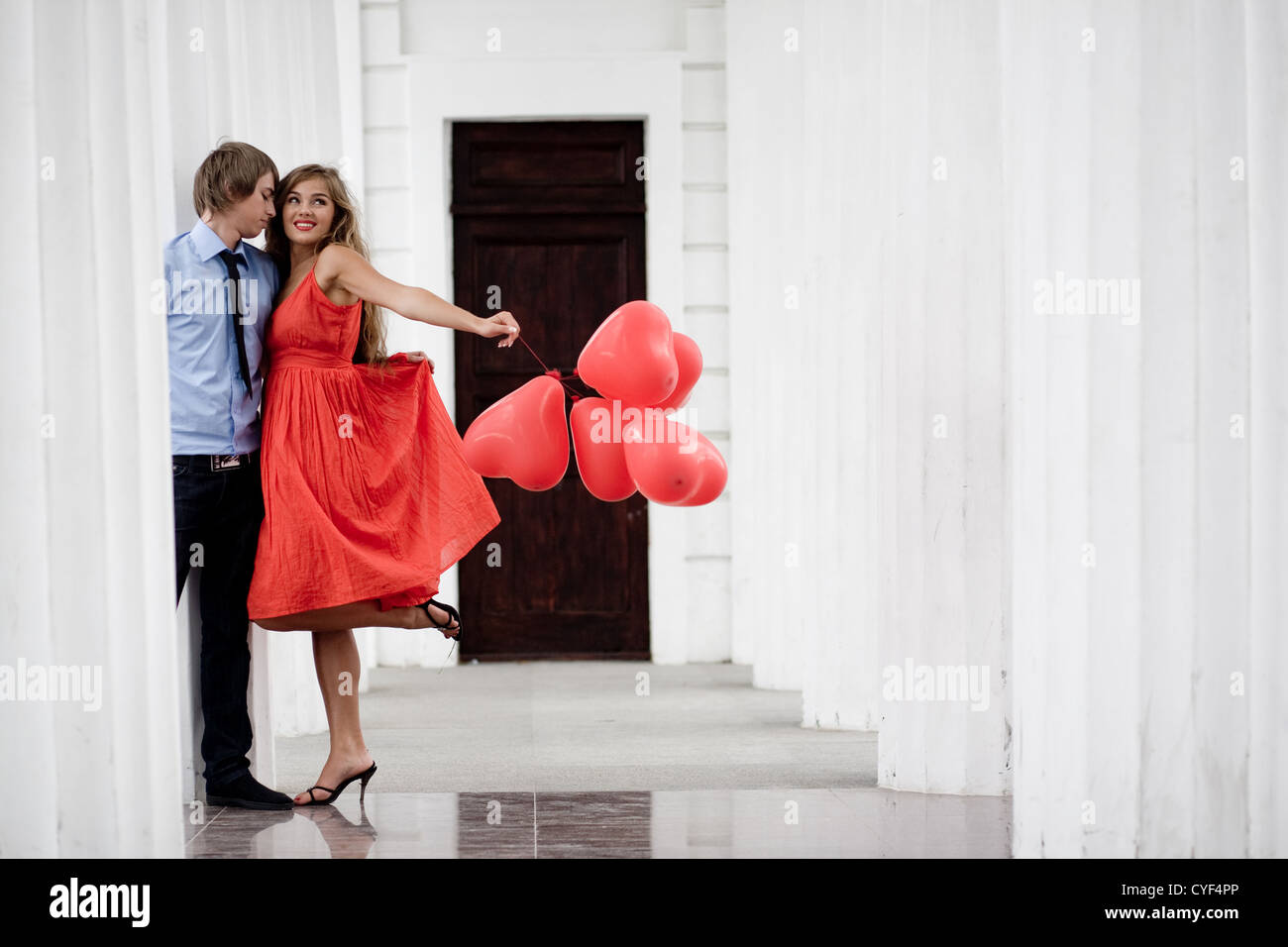 Coppia giovane kissing tra colonne bianche e azienda mazzetto di baloons-cuori Foto Stock