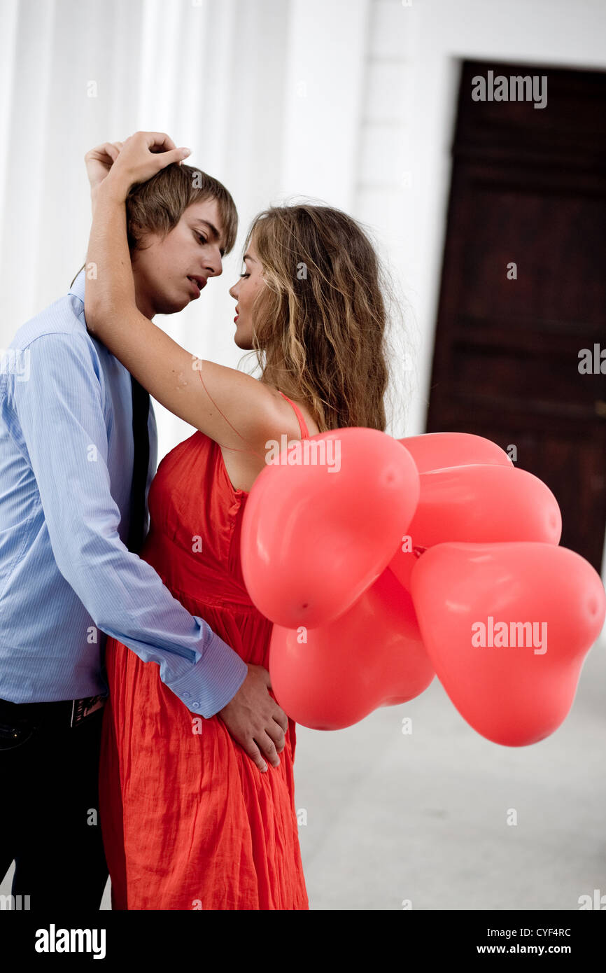 Coppia giovane baciando e abbracciando tra colonne bianche e azienda mazzetto di baloons-cuori Foto Stock