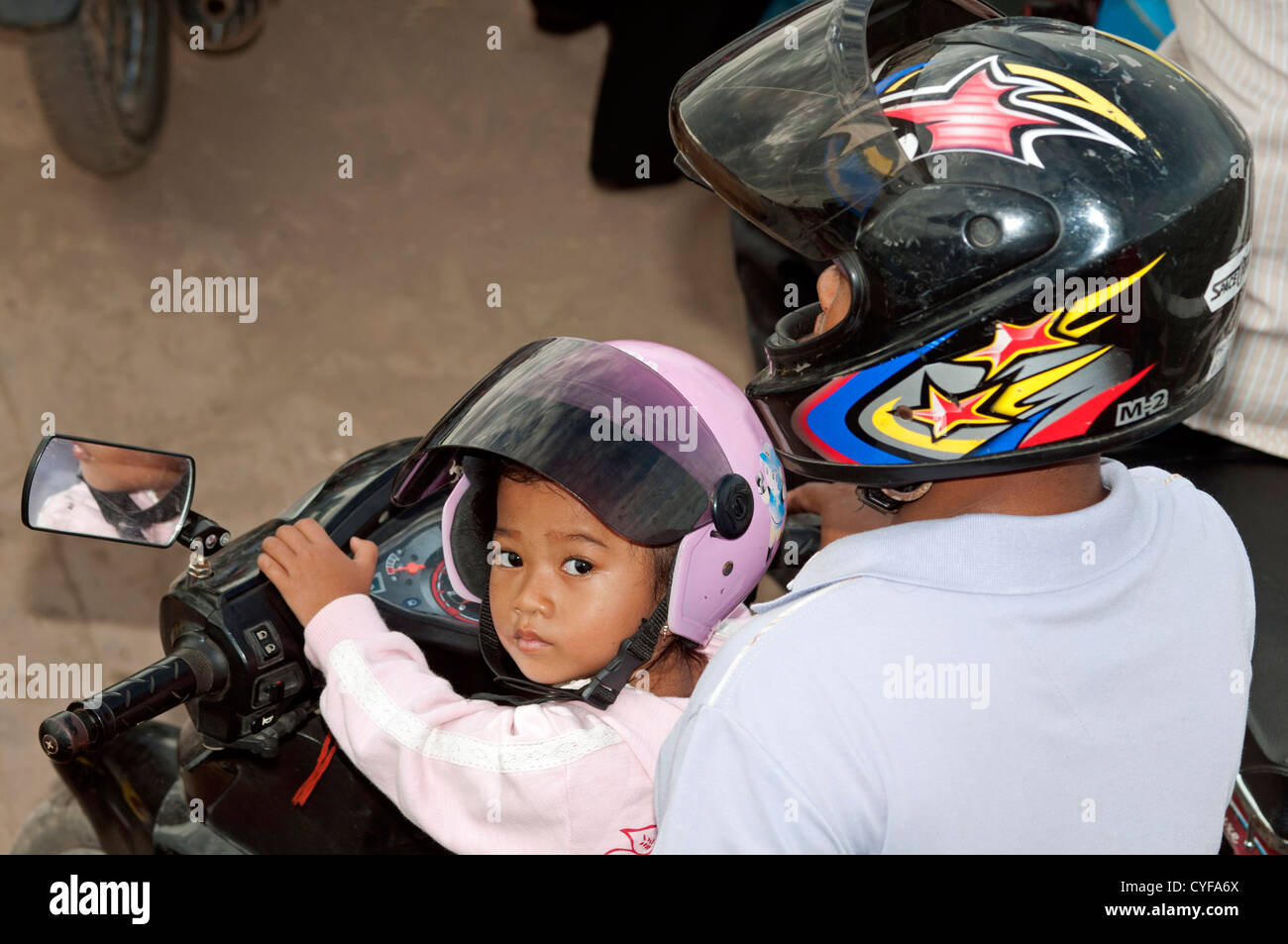Padre con figlia piccola su una moto che indossa caschi di protezione, Phnom Penh Cambogia Foto Stock
