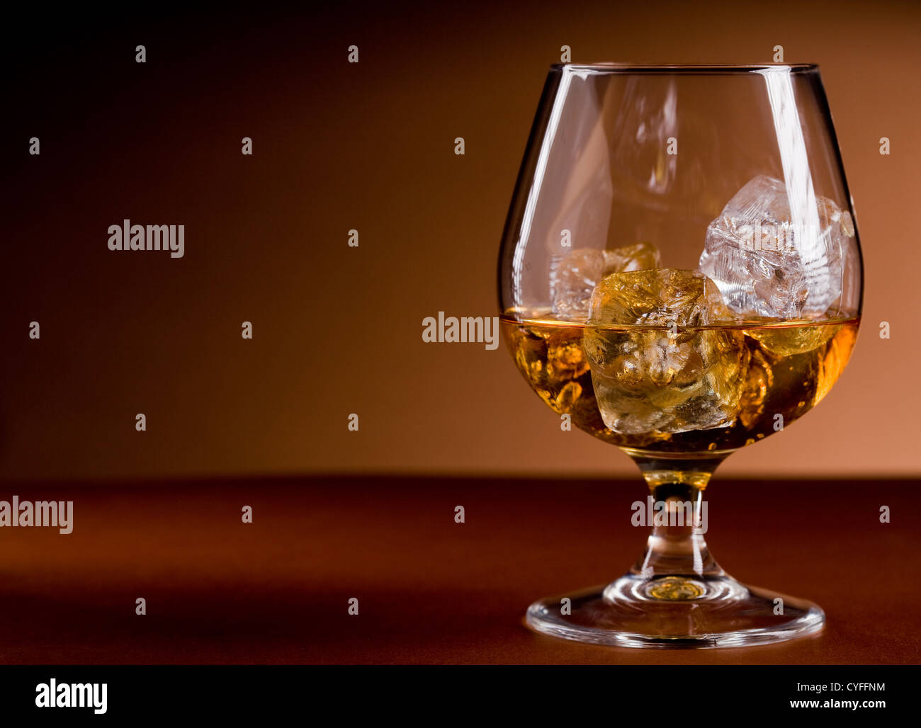 Foto di delizioso bicchiere di whiskey cognac con cubetti di ghiaccio su sfondo marrone Foto Stock