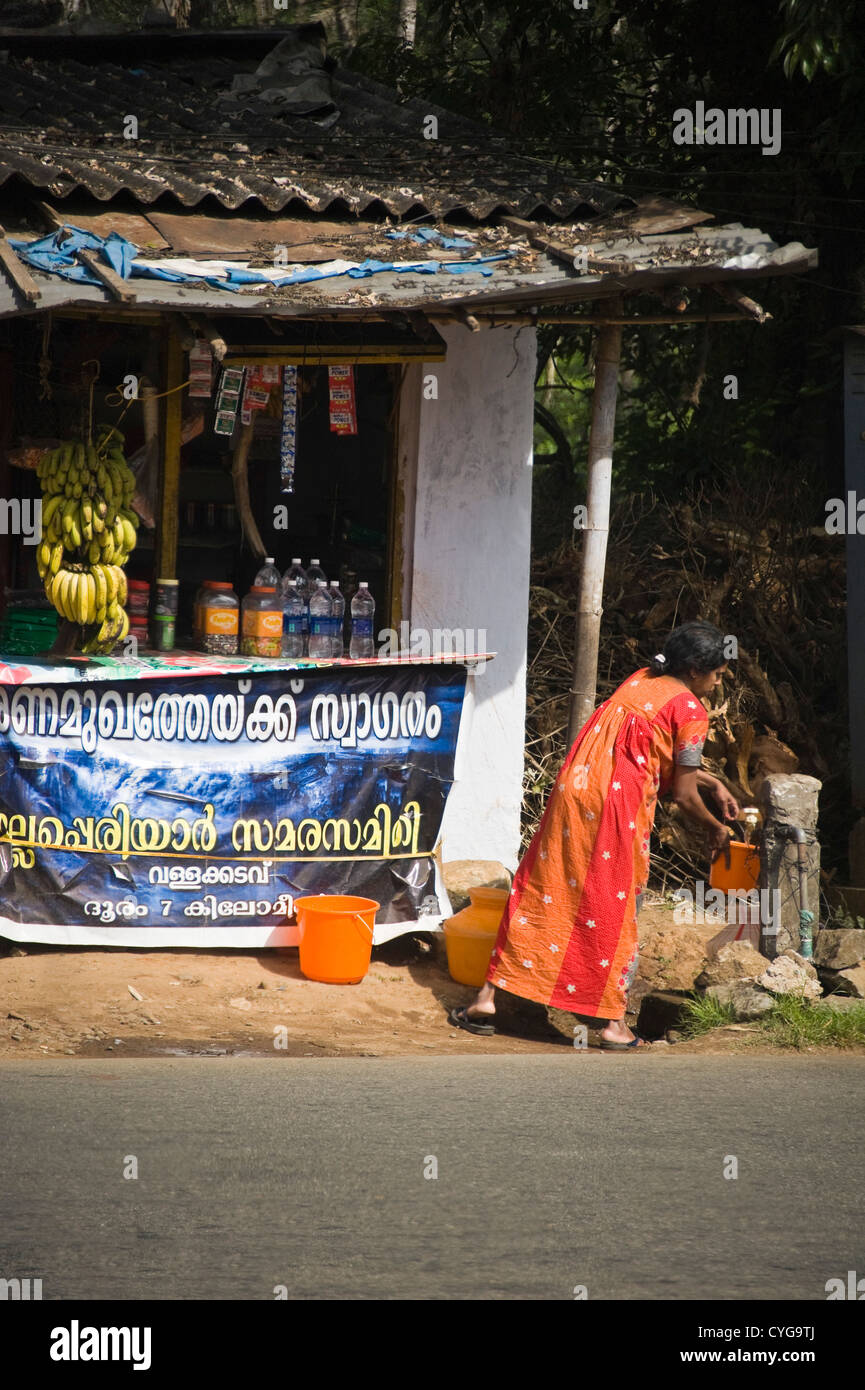 Ritratto verticale locale di donna indiana la raccolta di acqua fresca da un tubo montante nel mezzo di una tipica strada in Munnar. Foto Stock