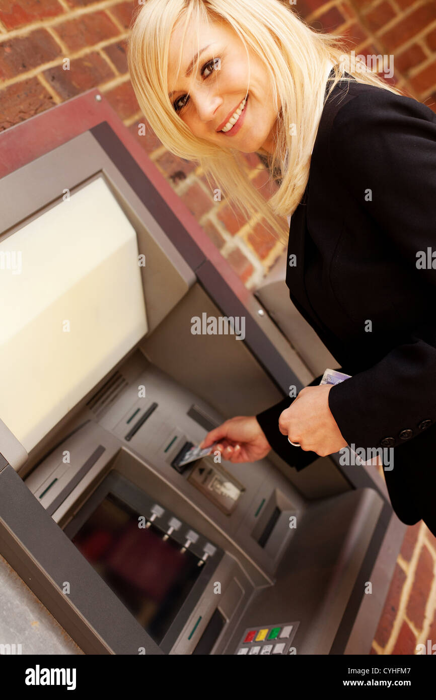 Smiley una splendida bionda mettendo la sua carta di credito in contanti macchina cercando di ritirare dei contanti Foto Stock
