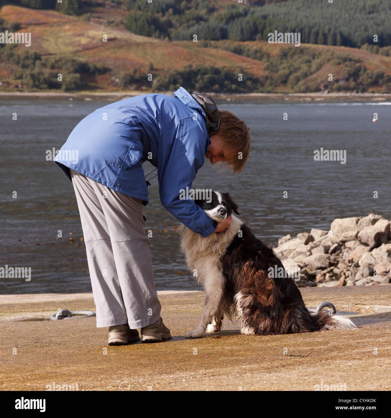Donna in Blue Coat con il bianco e nero Border Collie cane da mare, Glenelg, Scotland, Regno Unito Foto Stock