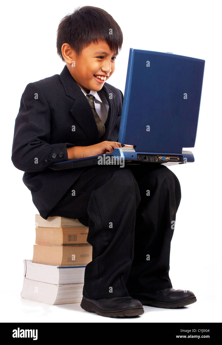 Ragazzo sul suo computer di studio per la scuola e seduto su una pila di libri Foto Stock