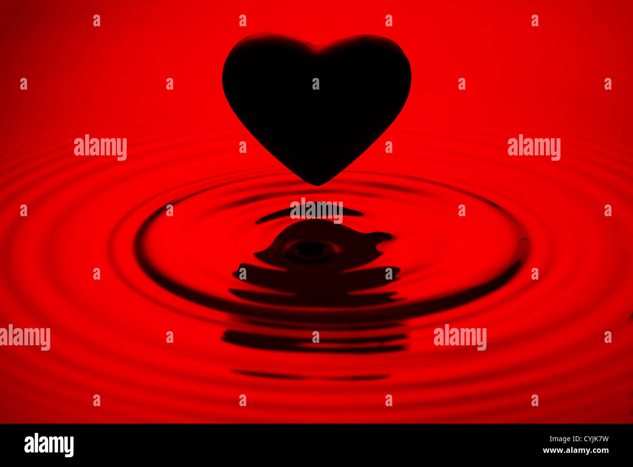 Cuore nero siluett su rosso acqua increspature sfondo Foto Stock