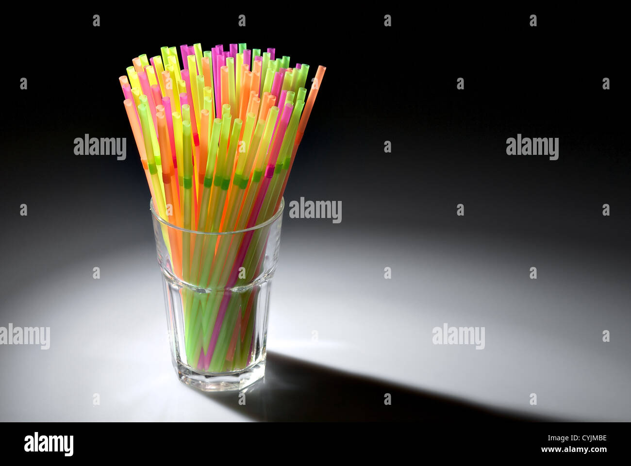 Flessibile multicolore cannucce in vetro in spot di luce isolati su sfondo nero Foto Stock