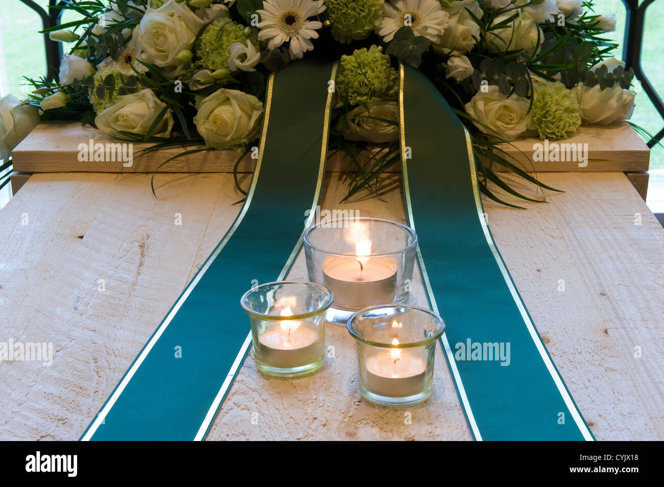 Una bara in un crematorio con una disposizione di fiori e candele accese su di esso Foto Stock