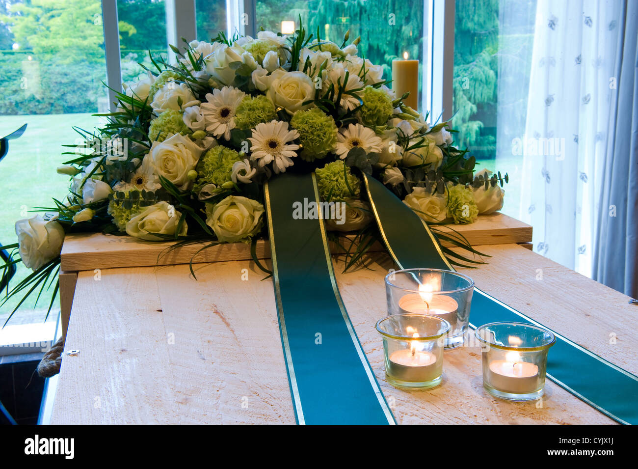 Una bara in un crematorio con una disposizione di fiori e candele accese su di esso Foto Stock