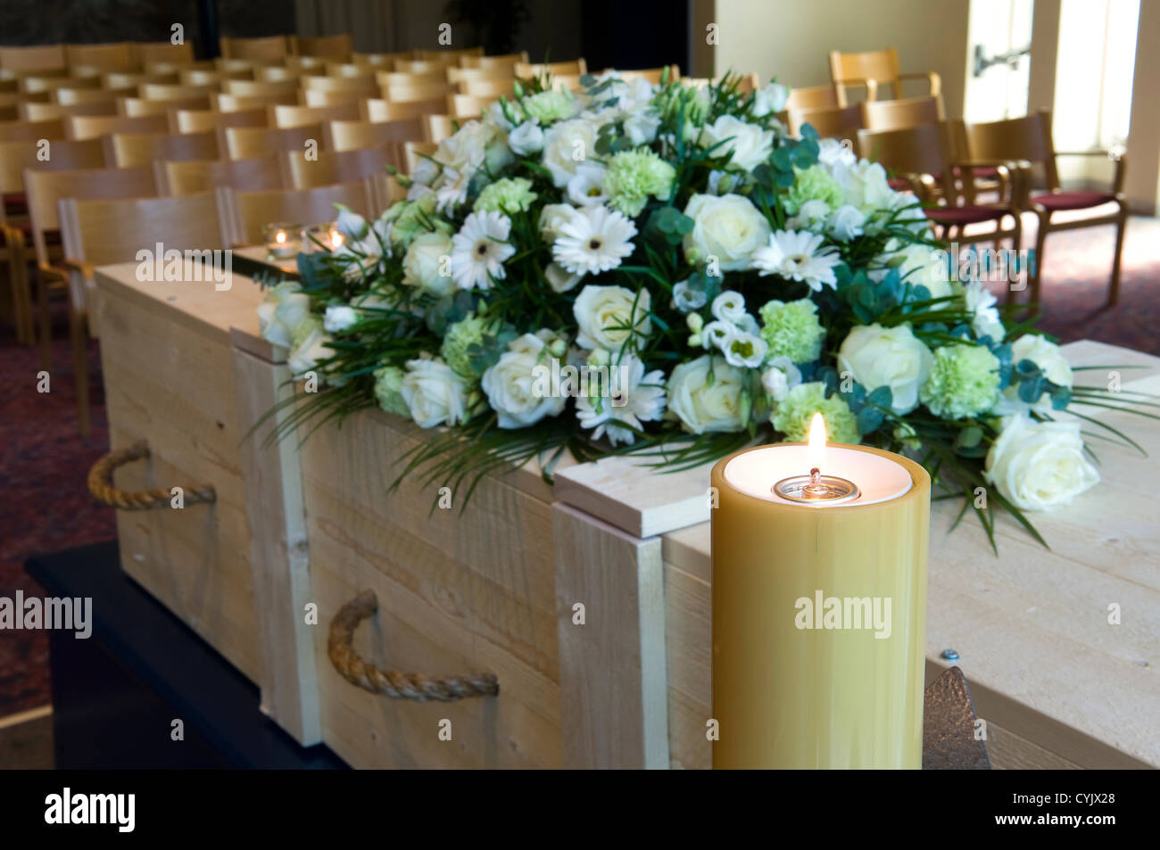 Una bara in un crematorio con un omaggio floreale e una candela che brucia Foto Stock