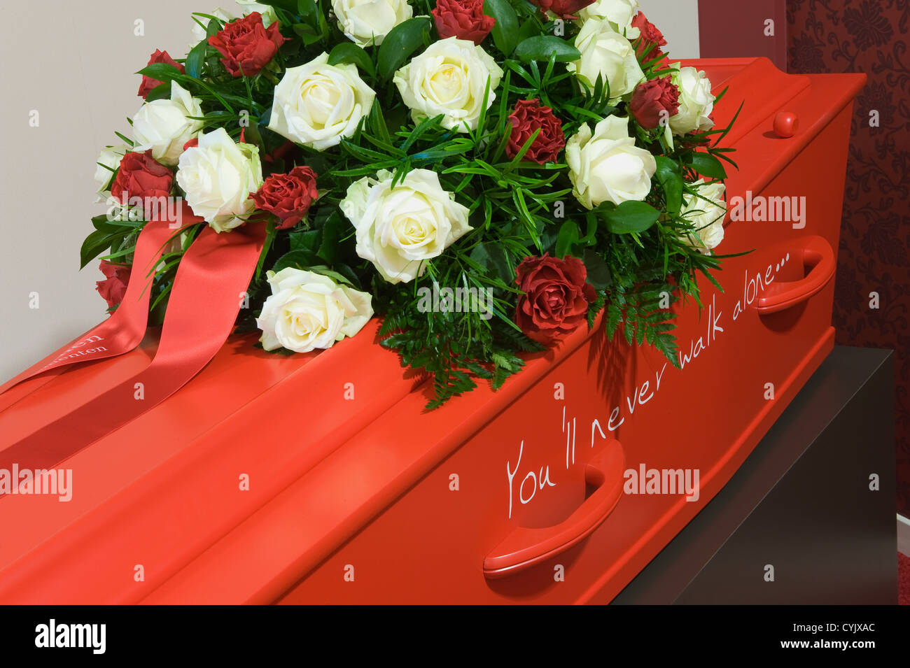 Una bara di rosso in un obitorio con un omaggio floreale Foto Stock