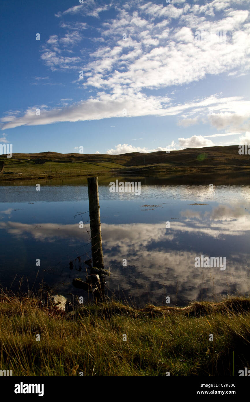Un vecchio post con un po' di scherma arrugginito attaccato sorge in acqua di mare, con nuvole bianche si riflette nell'acqua intorno ad esso Foto Stock