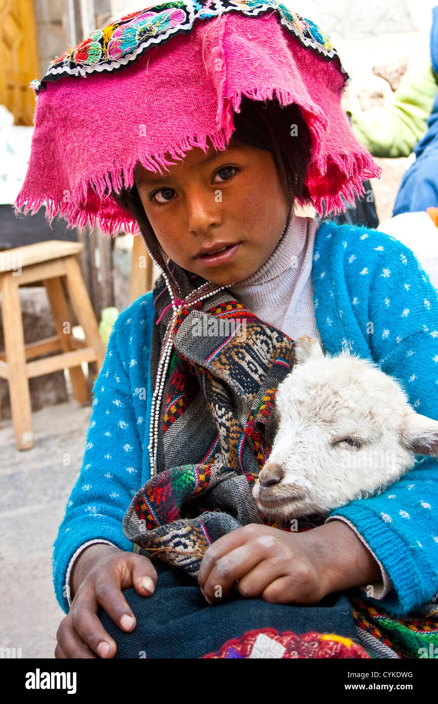 Pisac, Perù, una ragazza vestita in abbigliamento tradizionale pone con il suo lamb come la sua famiglia vende la loro mercanzia in Valle Sacra. Foto Stock