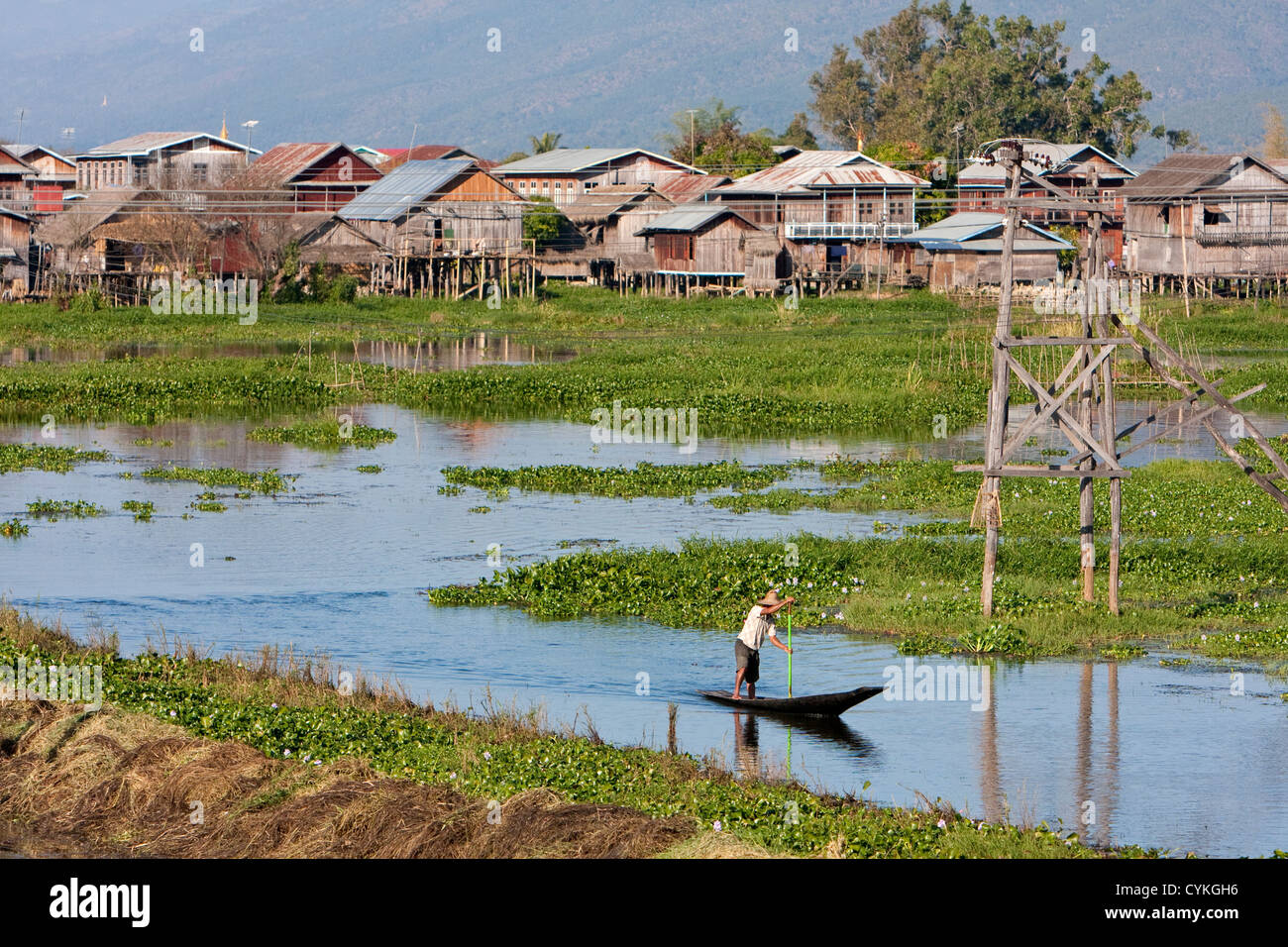 Myanmar Birmania. Uomo birmano pagaie sua canoa attraverso il villaggio fluviale, Lago Inle, Stato di Shan. Foto Stock