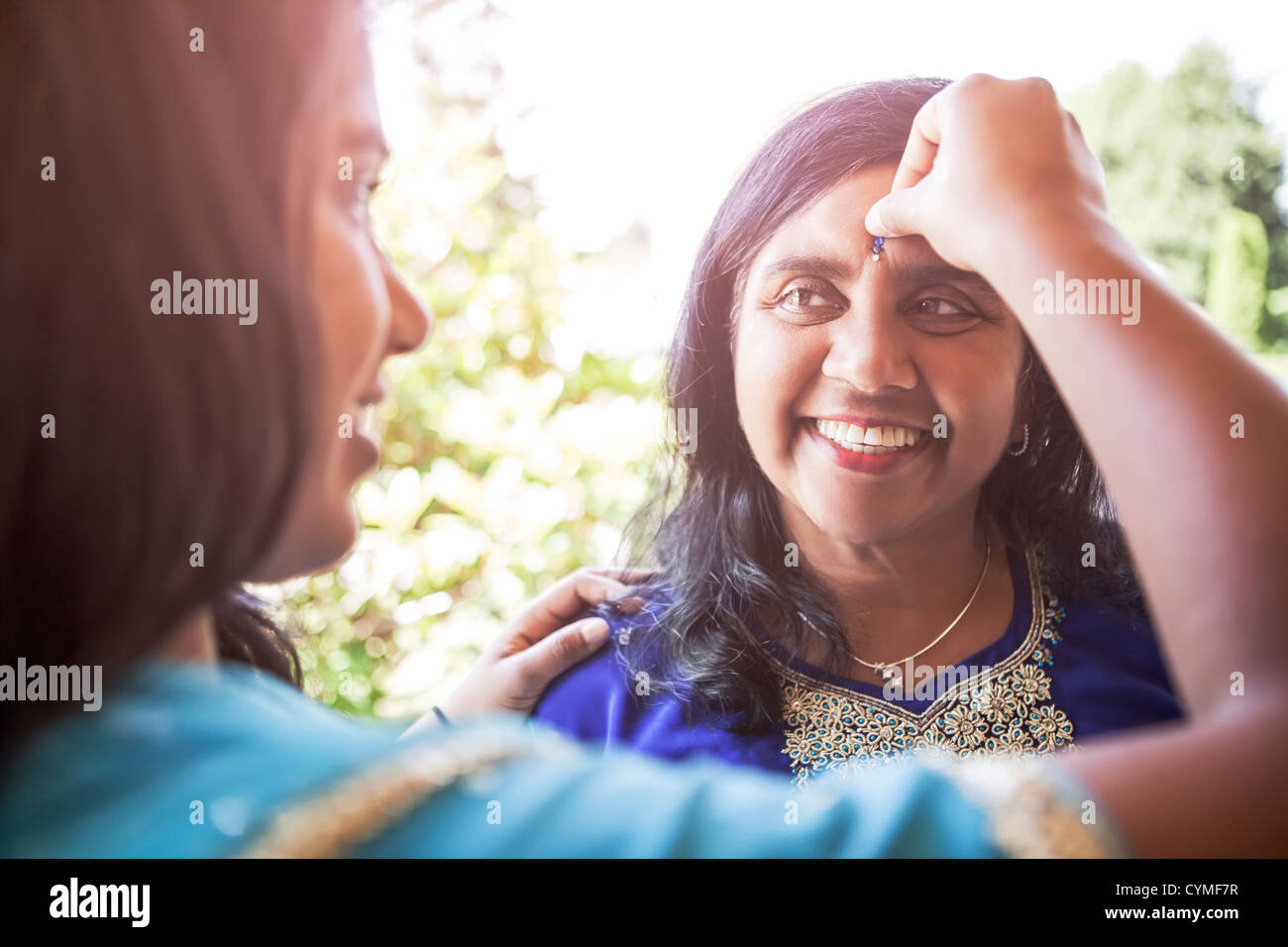 Donna indiana mettendo gioiello su madre di fronte Foto Stock