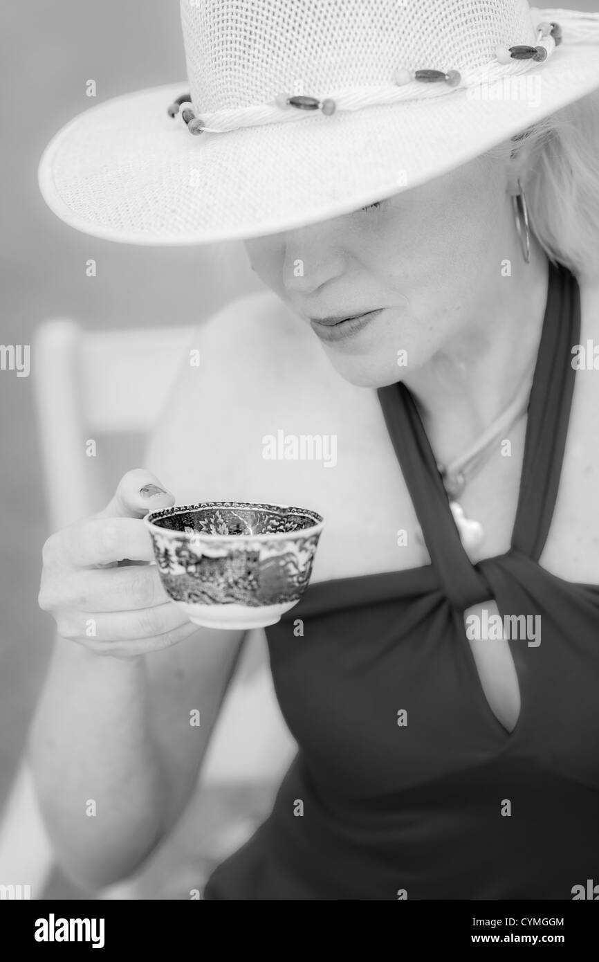Una signora con un cappello beve un caffè, close up e immagine in bianco e nero Foto Stock