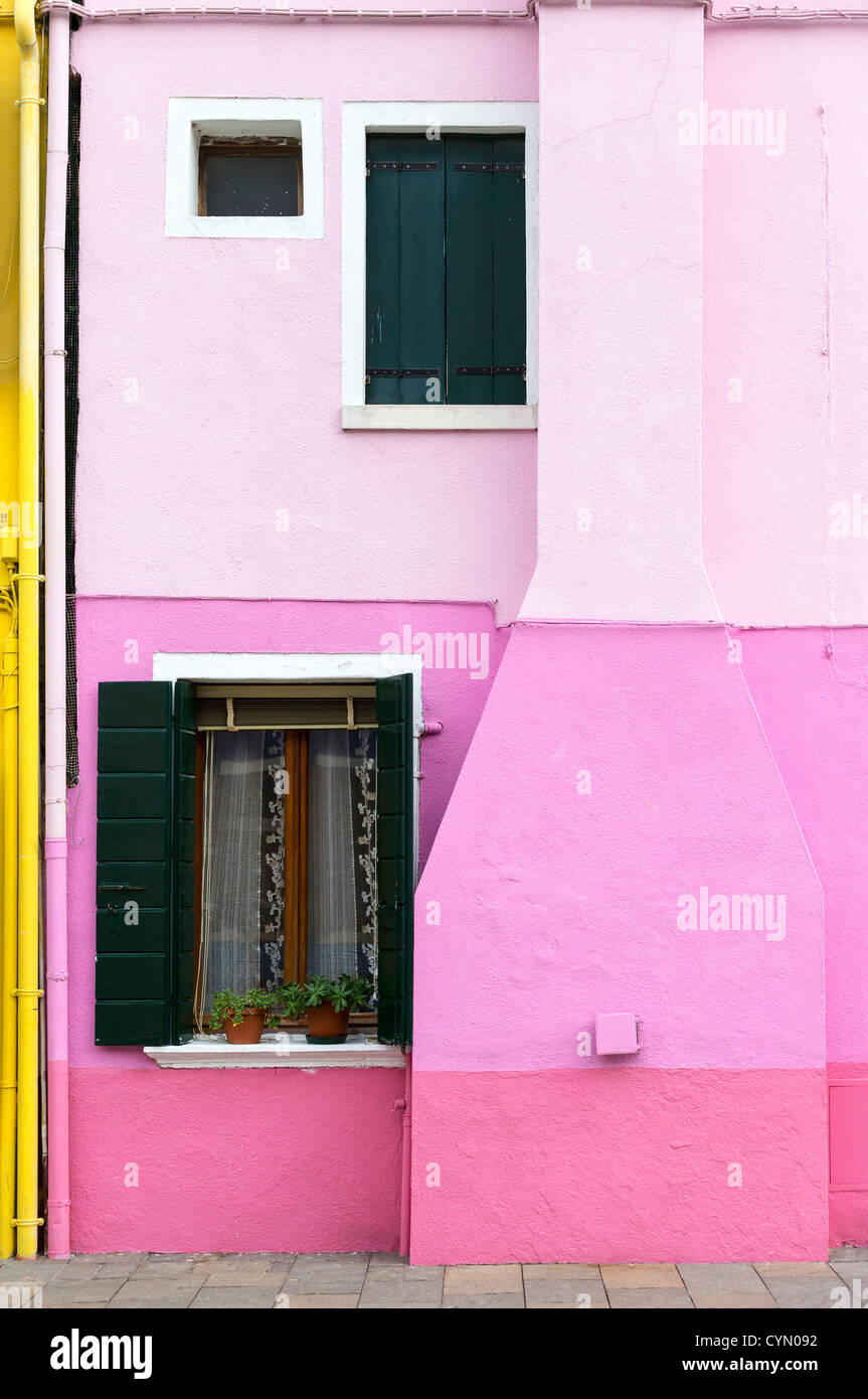 Un stranamente-casa dipinta a Burano, Venezia, in varie sfumature di rosa in bande orizzontali, e il bordo giallo di next-porta. Foto Stock