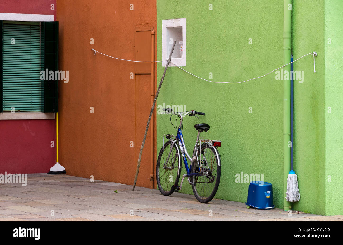 Un tipico contrasto di colori a Burano, Venezia, con una bicicletta e utensili domestici su un calce-parete verde con arancia dietro. Foto Stock